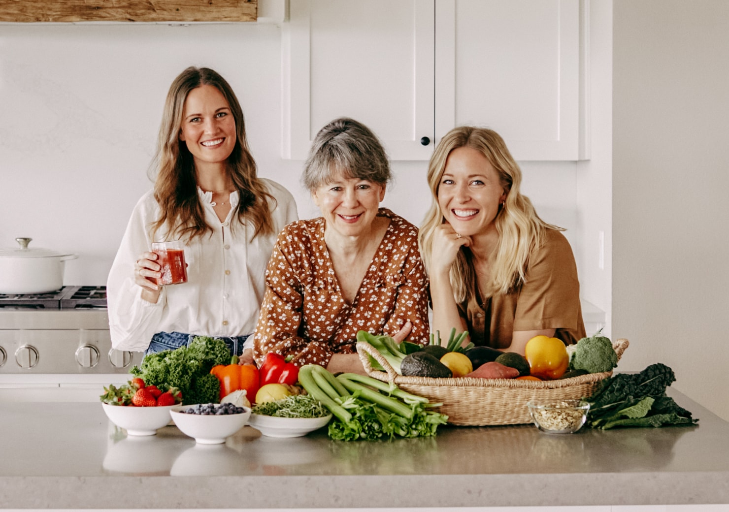A bright home kitchen with people and fresh produce.